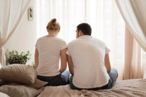 Couple assis de dos sur un lit, montrant le silence et la difficulté de parler de l’incontinence dans le couple